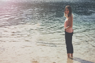 身穿粉色无袖上衣和黑色货裤的女子站在水面上